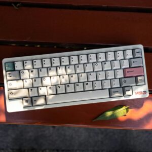 A compact white wireless keyboard on an outdoor wooden surface lit by natural sunlight.