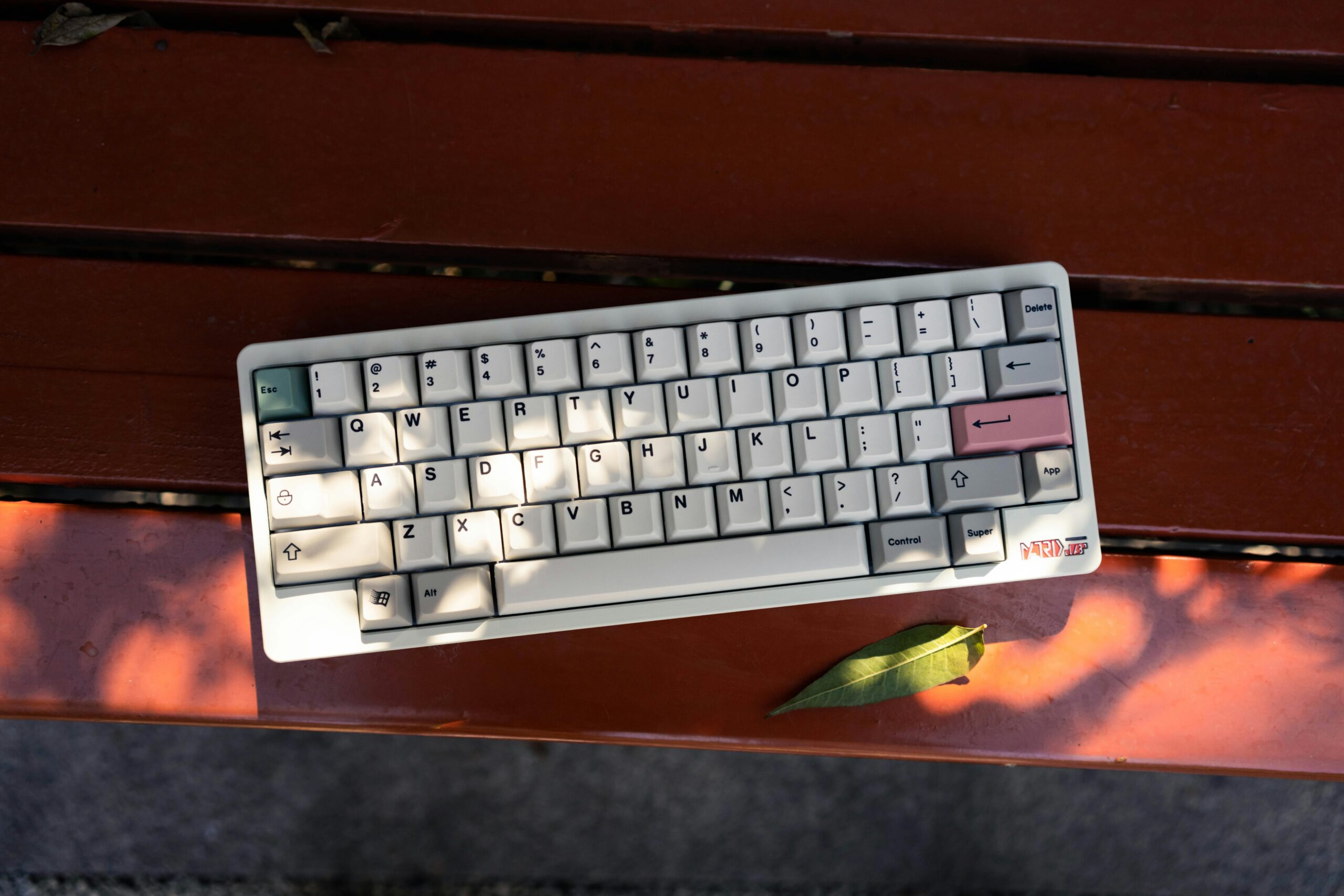 A compact white wireless keyboard on an outdoor wooden surface lit by natural sunlight.